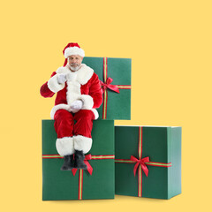 Portrait of Santa Claus with hot chocolate sitting on big gifts against yellow background