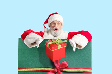 Portrait of surprised Santa Claus with gifts on light blue background
