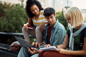 Young man using laptop while studying with female friend at campus.