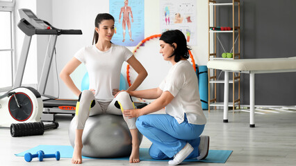 Mature physiotherapist working with young woman in rehabilitation center - obrazy, fototapety, plakaty