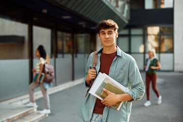 Young student in front of university building looking at camera. - obrazy, fototapety, plakaty