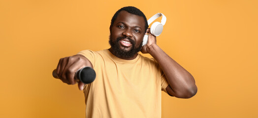 Male African-American singer with headphones and microphone on orange background