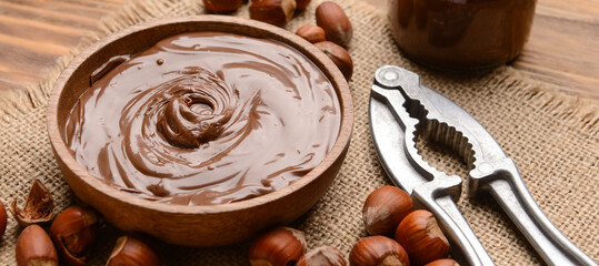 Bowl with tasty chocolate paste and hazelnuts on wooden background