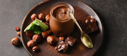 Jar with tasty chocolate paste and hazelnuts on dark background
