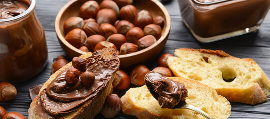 Bread with tasty chocolate paste and hazelnuts on dark wooden background, closeup
