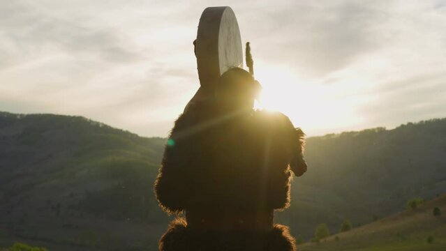 Silhouette of man conducting battle victory ceremony with shaman drum against mountains backside view. Siberian land mystical rituals. Altai culture