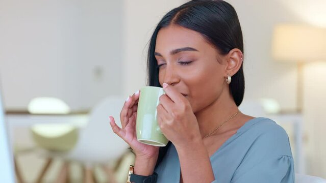 Business woman enjoying coffee or tea break while working in a modern office. Young worker feeling relaxed, taking a moment to enjoy a refreshing, tasty drink while reading and responding to emails