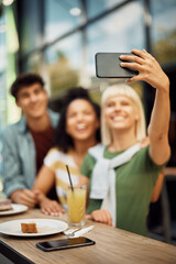 Close up of friends taking selfie with cell phone in cafe.