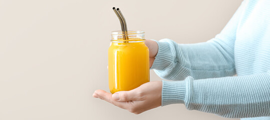 Woman with mason jar of healthy turmeric drink on light background