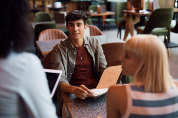 Young man and his girlfriend making an order while talking to waitress in restaurant.