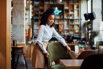 Young black waitress setting the tables in restaurant.