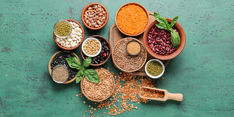 Different raw legumes with spices on green background