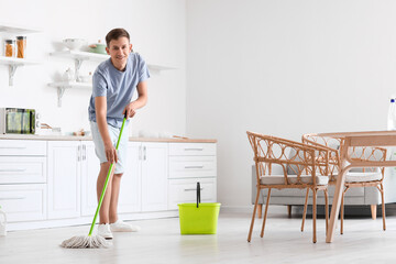 Handsome young man mopping floor in modern kitchen