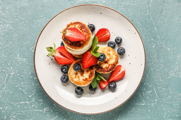 Plate with delicious cottage cheese pancakes, berries and mint leaves on green background