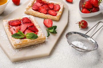Board with sugar powdered puff pastry and strawberry on light table - obrazy, fototapety, plakaty