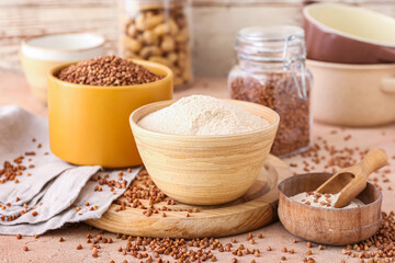 Board with bowls of flour and buckwheat grains on beige background