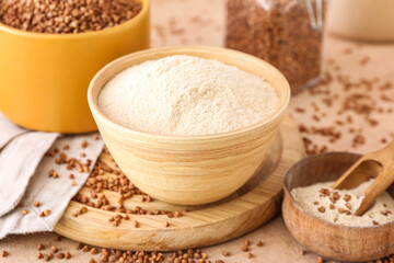 Board with bowls of flour and buckwheat grains on beige background