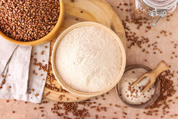 Board with bowls of flour and buckwheat grains on beige background
