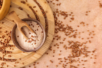 Board with bowl of flour, scoop and buckwheat grains on beige background
