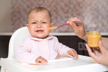 A crying baby refuses to eat. Baby food. A cranky child. real motherhood. Feeding the baby from a...