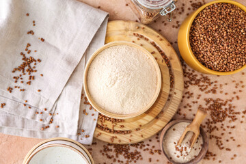 Obraz na płótnie Canvas Board with bowls of flour and buckwheat grains on beige background