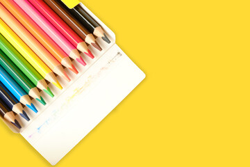 Multi-colored pencils for drawing in a box on yellow background with place for text. - Powered by Adobe