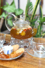 Chamomile tea in a glass teapot with cups and crystalized fruits wooden table