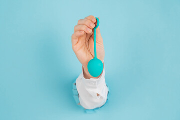 A woman's hand sticks out of a hole in a blue background and holds a vaginal egg. 