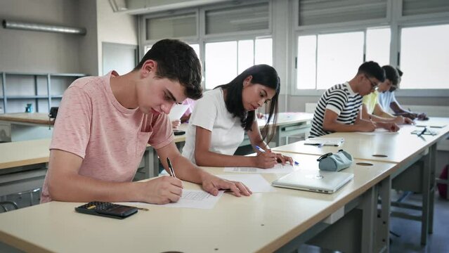 Group of high school teenager students taking math exam at classroom - Latin American Girl and Caucasian Boy writing test 