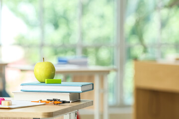 Apple with school books and stationery supplies on table in classroom