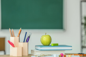 Apple with school books and stationery supplies on table in classroom