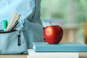 Apple with school books and backpack on table in classroom, closeup