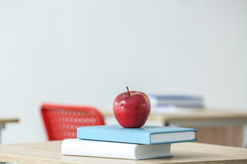 Apple with school books on table in classroom, closeup