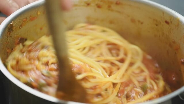 Cooking and stirring pasta alla norma.
