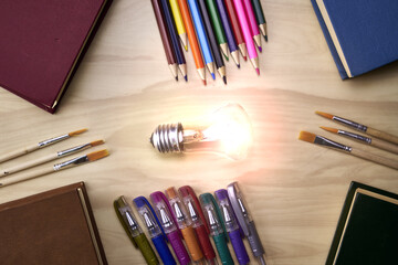 fountain pens pencils brushes books and a burning light symbolizing knowledge on the table concept education science