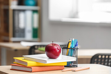 Apple with books, pen cup and school stationery on table in classroom