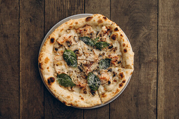 italian pizza with burnt sides on a wooden background top view. pizza with white truffles, mushrooms, basil leaves. sliced pizza close-up	