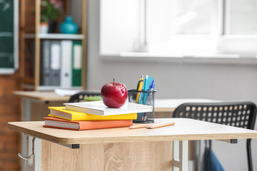 Apple with books, pen cup and school stationery on table in classroom