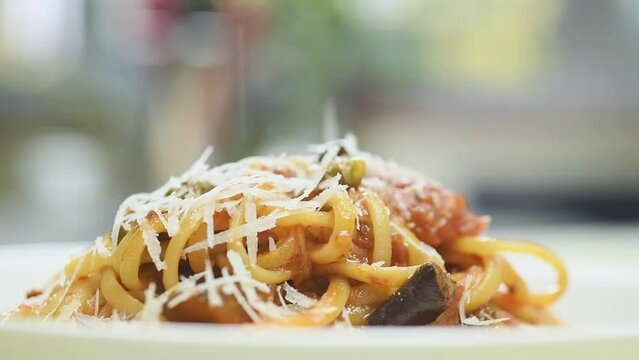 The chef sprinkles with parmesan Pasta alla Norma.
