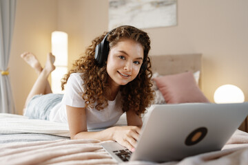 Portrait of a young curly woman using laptop in bed at home
