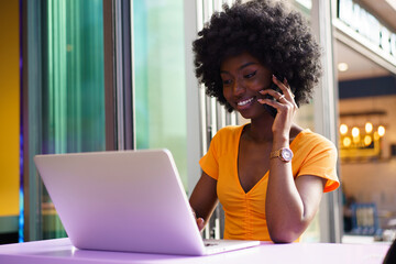 Fototapeta na wymiar Happy beautiful young black woman using laptop in cafe