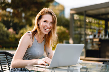 Happy beautiful young woman working on laptop in street cafe