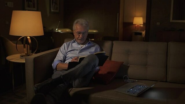 Night time, portrait of an elderly gray-haired architect with glasses writing down thoughts in a notebook, focused buisnessman on a business trip, the thinking process, loneliness.