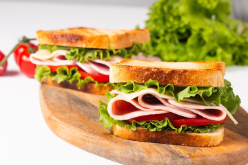Close-up of two toasted sandwiches with fresh ham, cheese and vegetables on background. Club sandwich and take-away concept. Fast food. 