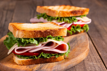 Close-up of two toasted sandwiches with fresh ham, cheese and vegetables on background. Club...
