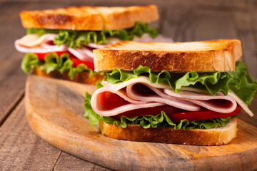 Close-up of two toasted sandwiches with fresh ham, cheese and vegetables on background. Club sandwich and take-away concept. Fast food. 