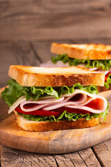Close-up of two toasted sandwiches with fresh ham, cheese and vegetables on background. Club sandwich and take-away concept. Fast food. 