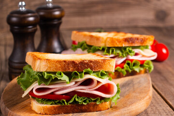 Close-up of two toasted sandwiches with fresh ham, cheese and vegetables on background. Club sandwich and take-away concept. Fast food. 