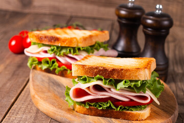 Close-up of two toasted sandwiches with fresh ham, cheese and vegetables on background. Club sandwich and take-away concept. Fast food. 