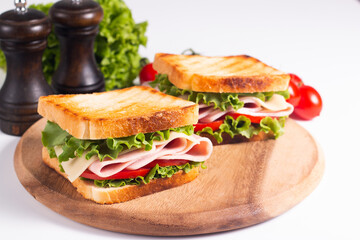 Close-up of two toasted sandwiches with fresh ham, cheese and vegetables on background. Club sandwich and take-away concept. Fast food. 
